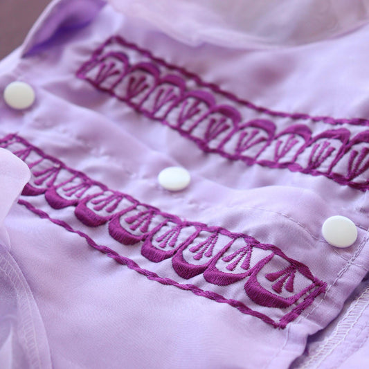 Close-up of a garment with purple embroidery and white buttons.